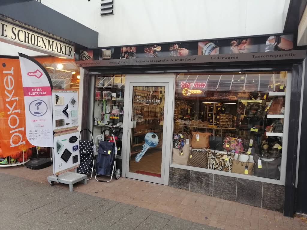 De winkelpui van De Schoenmaker in Winkelcentrum Hesseplaats, met tassen in de etalage en het bord Sleutelservice · Naamplaten · Schoenenreparatie & onderhoud · Lederwaren · Tassenreparatie
